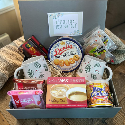 Gift basket with snacks, mugs, and cookies on a wooden surface